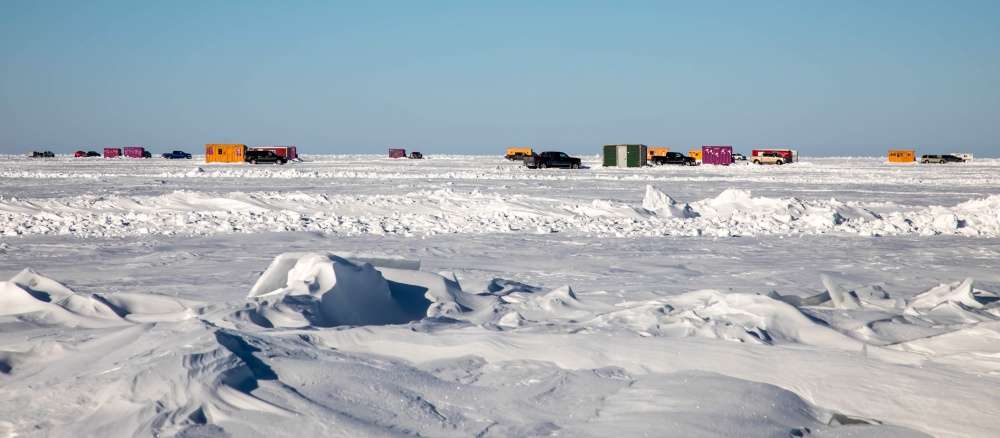 Frozen lake with ice houses and trucks in the distance.