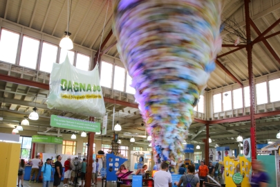 People looking at an exhibit of a large spinning "tornado" made of plastic bags with a sign that reads "Bagnado".