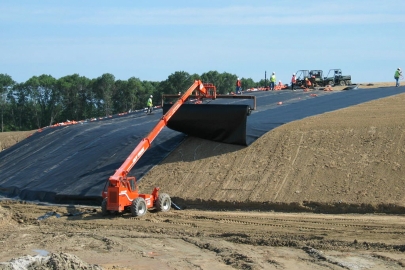 Equipment rolls black plastic sheet cover over soil at a closed landfill.