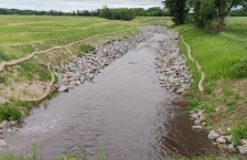 Water flowing through a shallow ditch with rock stabilized banks to prevent erosion. 
