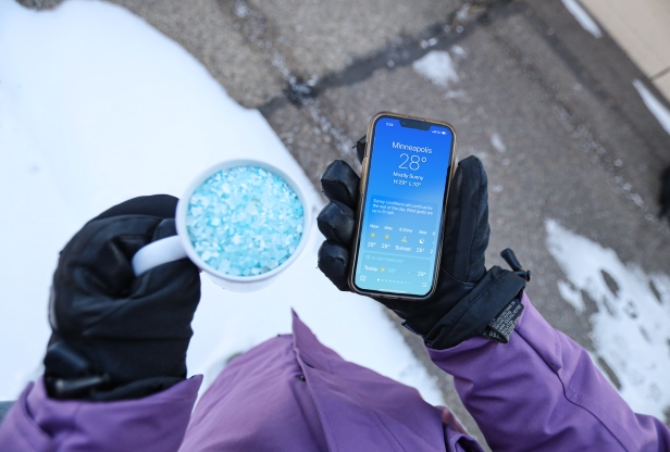 Person holding a cup of de-icing salt and a cellphone showing the temperature.