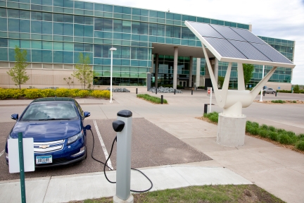 Electric car charging in front of office building next to solar panel.