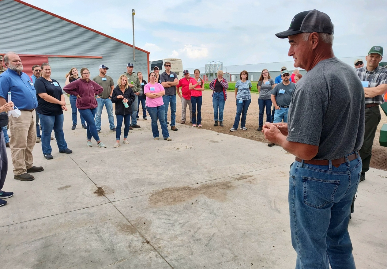 Don Tschida speaking to a group of people on a farm.