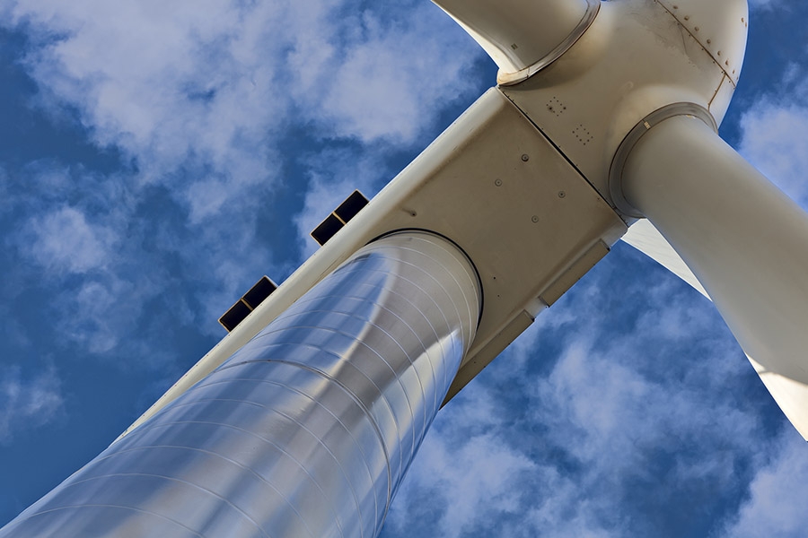 Looking up at a wind turbine with blue sky and some light clouds.