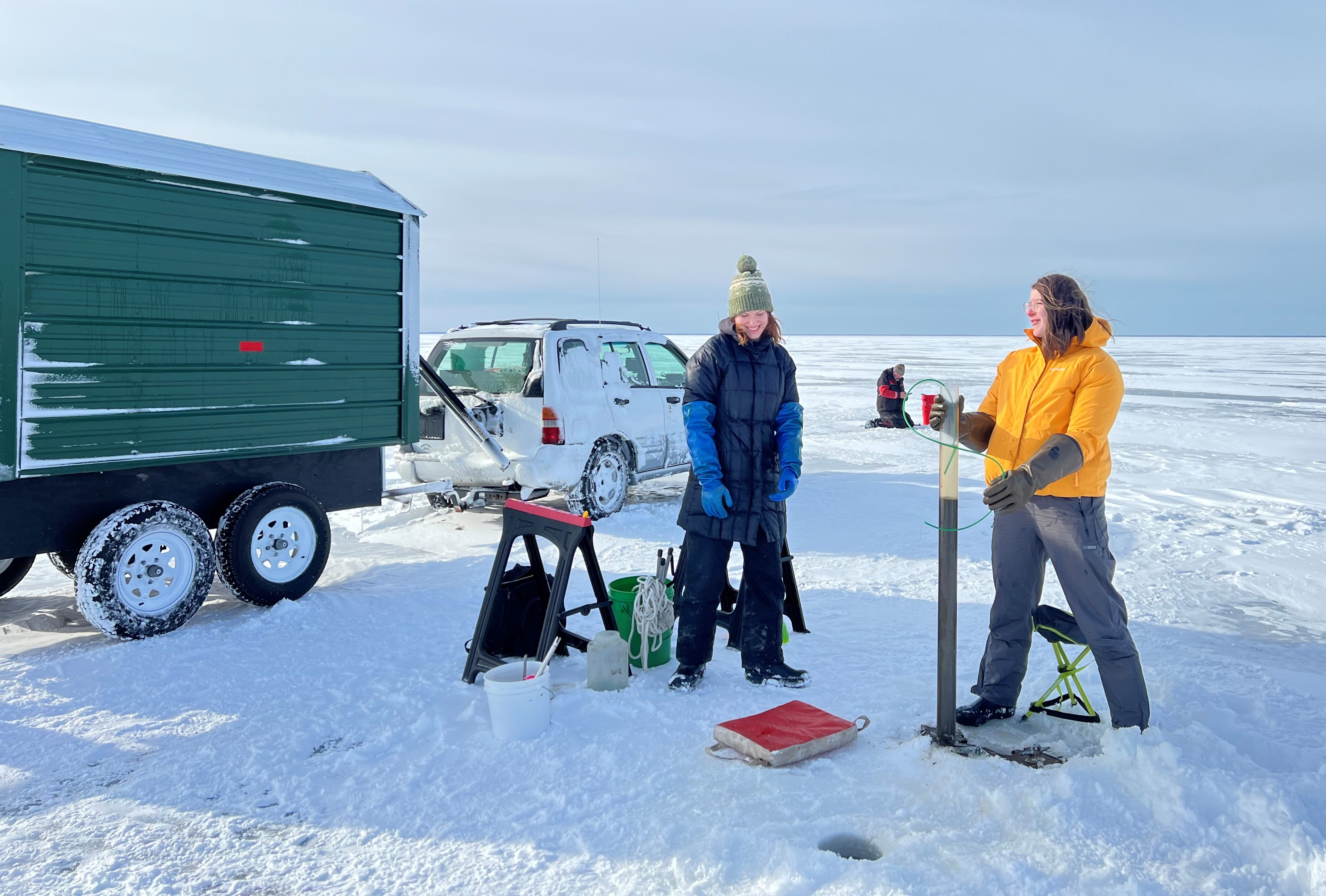 Researchers standing on a frozen lake and collecting samples of sediment from the bottom of the lake