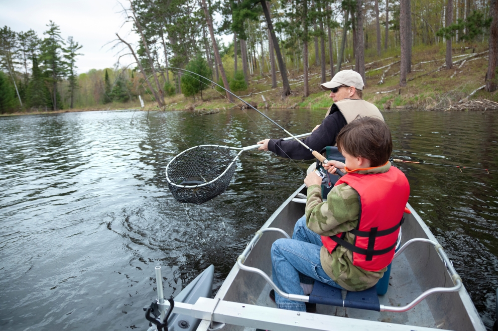 Father and son fishing in a boat on a lake.