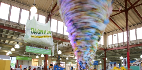 People looking at an exhibit of a large spinning "tornado" made of plastic bags with a sign that reads "Bagnado".