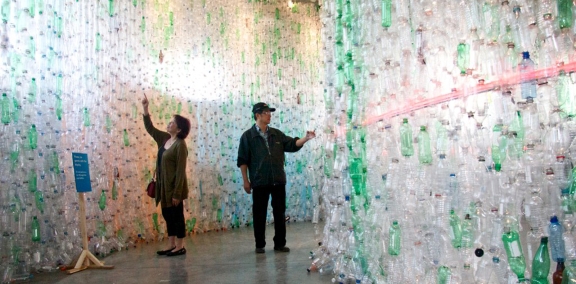 Two people walking between tall walls made of empty plastic bottles.