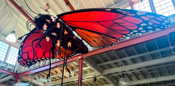 Large model of a monarch butterfly suspended from the ceiling of an exhibit hall.