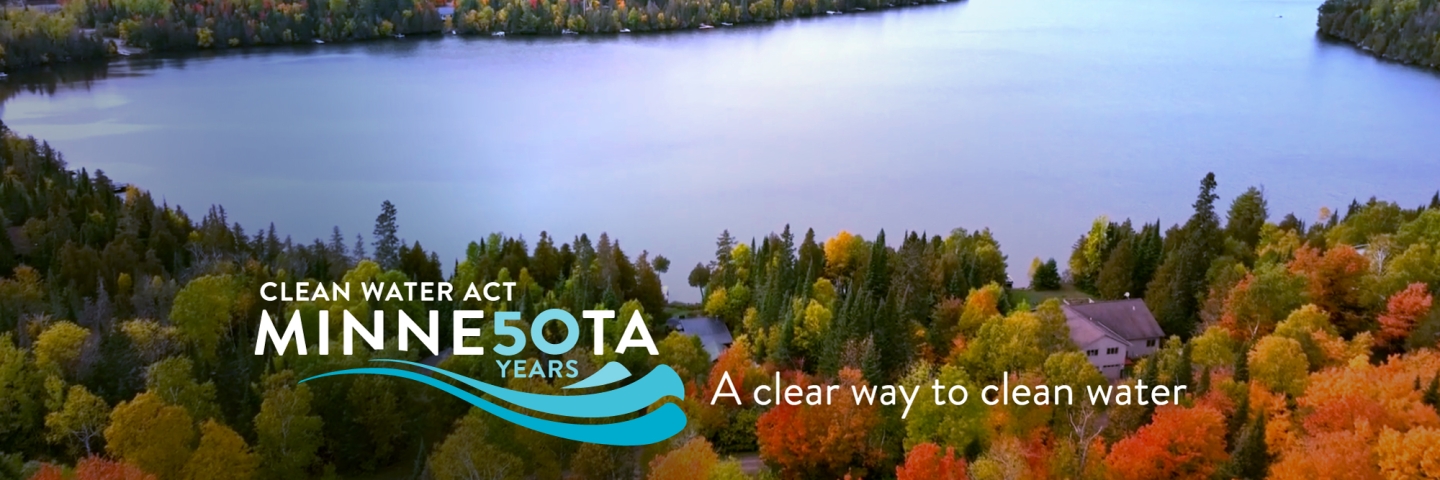 A Minnesota lake surrounded by a forest with autumn colors a few houses can be seen on along the lake.