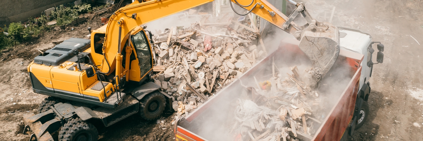 Excavator loading construction waste into truck with its bucket.