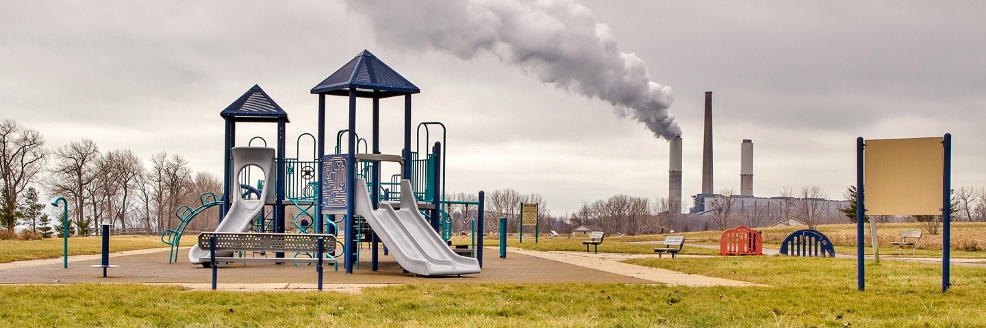 Children's playground with smokestacks emitting smoke in the background.