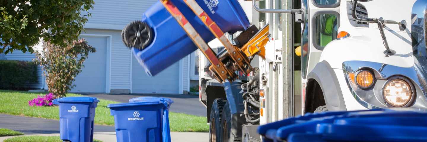 Recycling truck lifting up container along neighborhood curb.