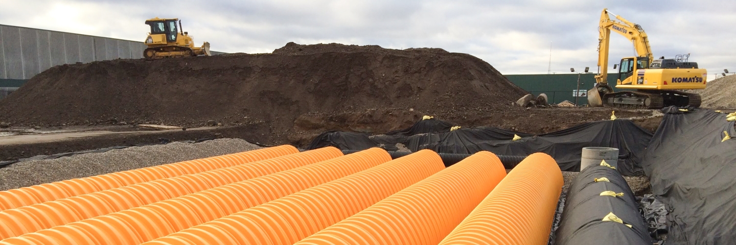 Construction yellow large corregated pipes being placed under ground as part of stormwater retention project.