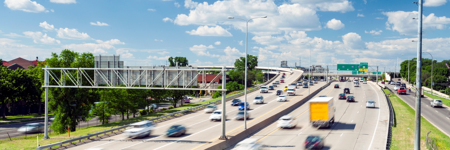 Light traffic on a freeway under a blue sky with white puffy clouds.