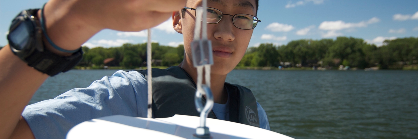 Close up of young Asian man by a lake holding up a Secchi disk.