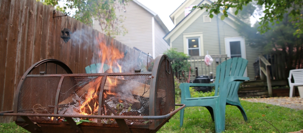 Green lawn chairs face smoky fire pit in backyard