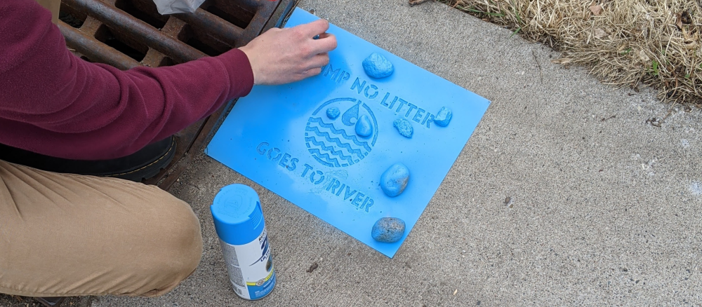 Person using a stencil to promote keeping litter out of a storm drain