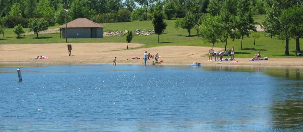 View from the lake looking toward people in the distance on a sandy beach and wading in the water.