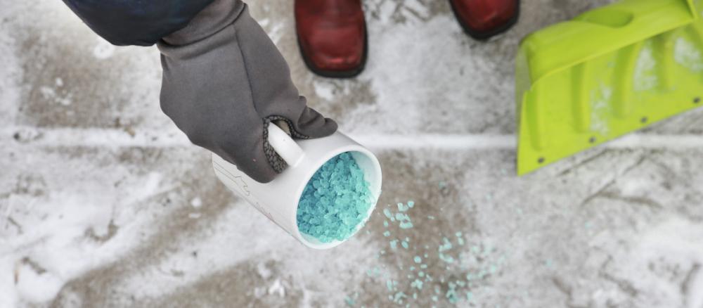 Pouring salt from a coffe mug on icy sidewalk