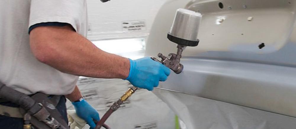 A worker in an auto body shop paints a car using a water-borne finish.