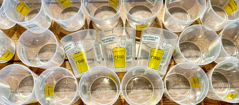 Overhead view of rows of empty translucent plastic cups, three are turned on their sides and say "Please return me, I'm reusable!"