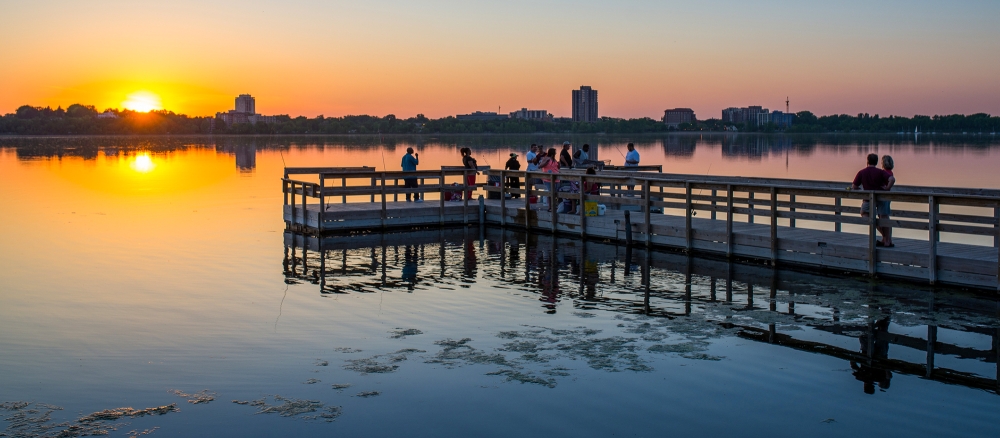 People gathered on a large dock on a still lake at sunset.