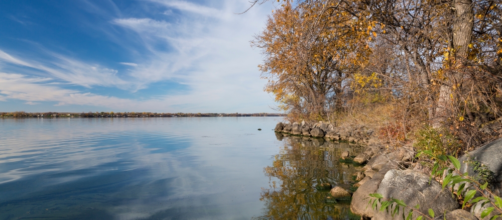 Calm lake reflecting wispy clouds along a rocky shoreline in autumn.