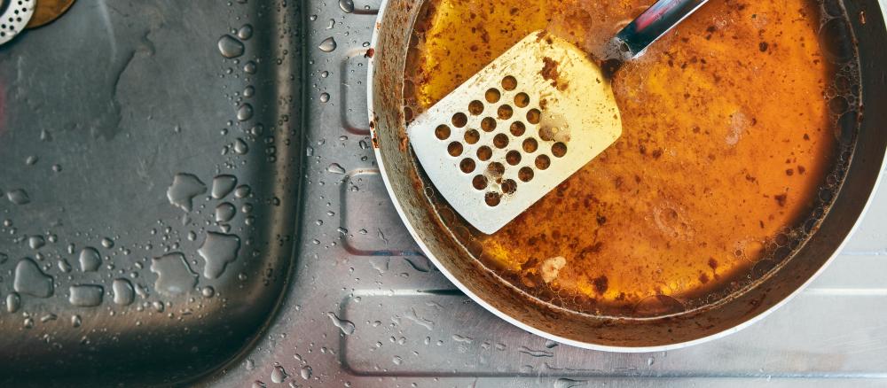 An overhead view of a spatula in a pot filled with grease sitting alongside a sink