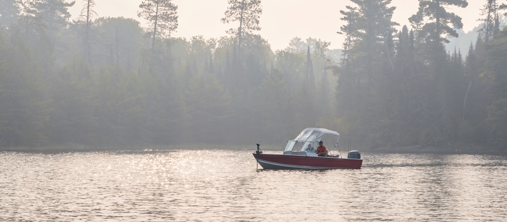 Fishing boat on a calm lake with a hazy tree-lined shore in the background. 