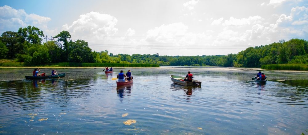 People in four canoes and a small fishing boat on a lake.