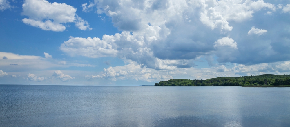 Blue sky with puffy white clouds over a large, still lake.