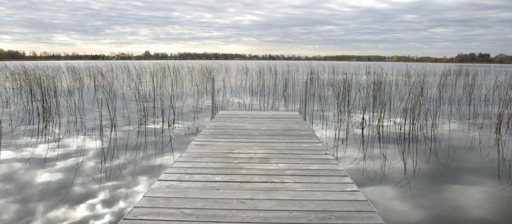Dock in lake with water reflecting grey cloudy skies.