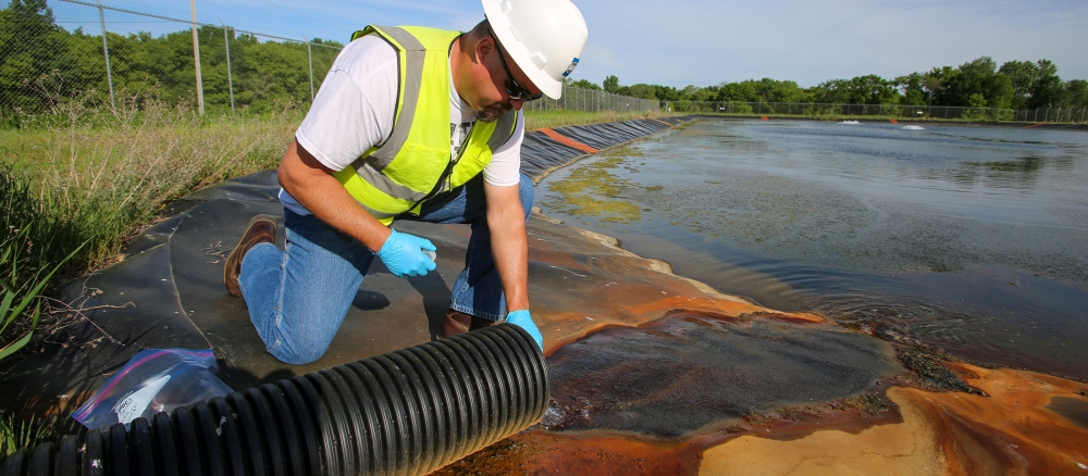 Worker in hard hat and gloves collects water sample.