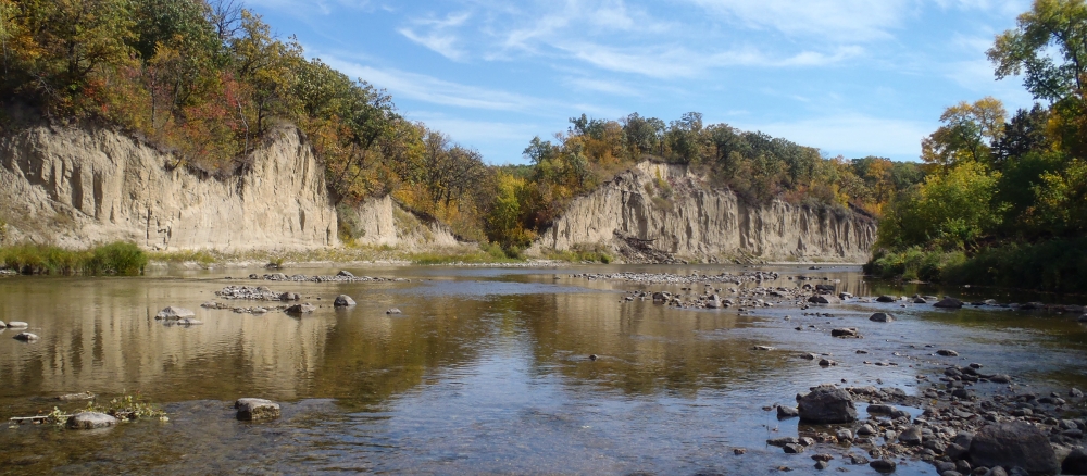 Tall, exposed rock banks line a shallow, rocky river. 