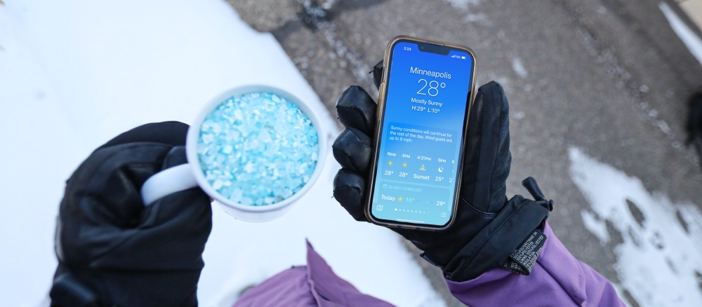 Person holding a cup of de-icing salt and a cellphone showing the temperature.