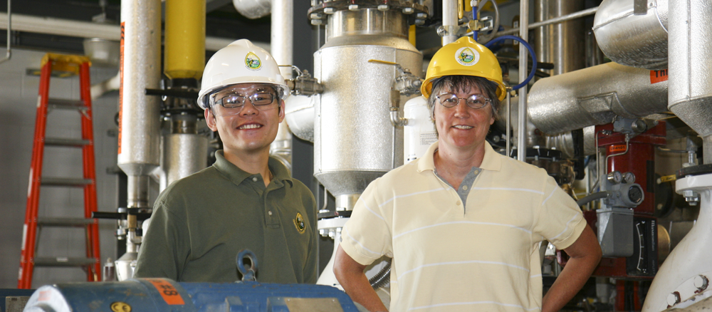 Two people in an industrial setting wearting hard hats