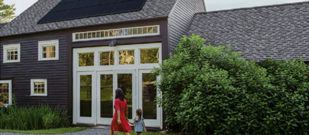 A woman and young girl holding hands and walking to the front door of a house with a solar panel on the roof.