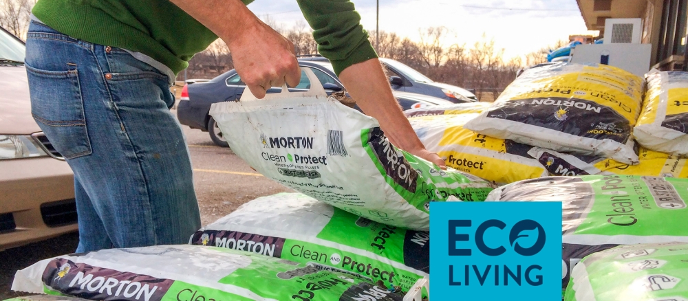 A man lifts a bag of water softener pellets from a pile of bags.