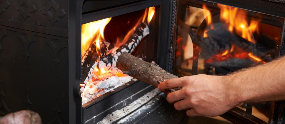 A hand putting a piece of wood into the front door of a wood-burning stove