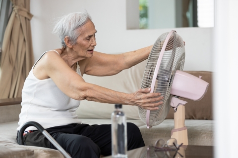 Senior woman enjoying breeze from electric fan.