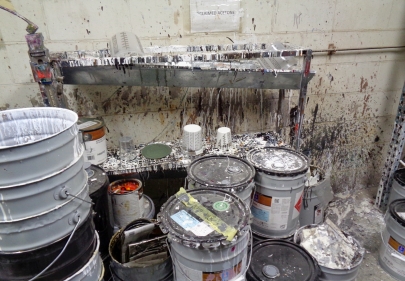 Paint splattered stacks of open and closed five gallon buckets and cement walls.