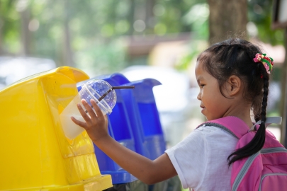Young Asian girl throwing away plastic cup in recycling container.