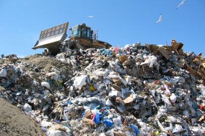 A landfill compactor on top of a mound of garbage in a landfill.