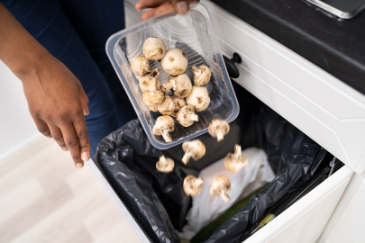 Woman throwing old mushrooms into garbage bin.