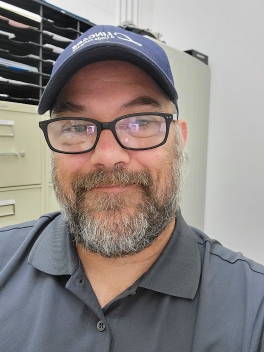 Headshot of James Wooton, a man with a beard wearing glasses and a cap.