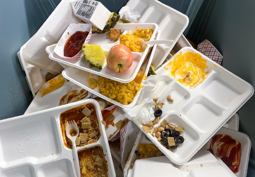 Disposable lunch trays and uneaten food in a waste bin. 
