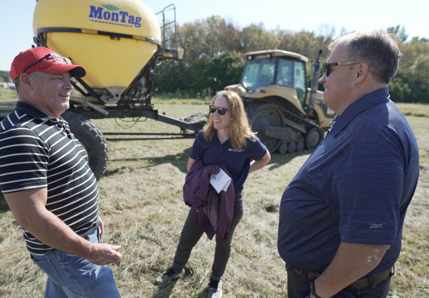 Two men and a woman having a conversation standing next to farm equipment.
