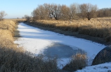 Small frozen stream running through wetland in winter.