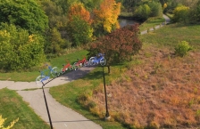 A bicycle sculpture forms a gateway to a paved trail that runs through colorful trees next to a river